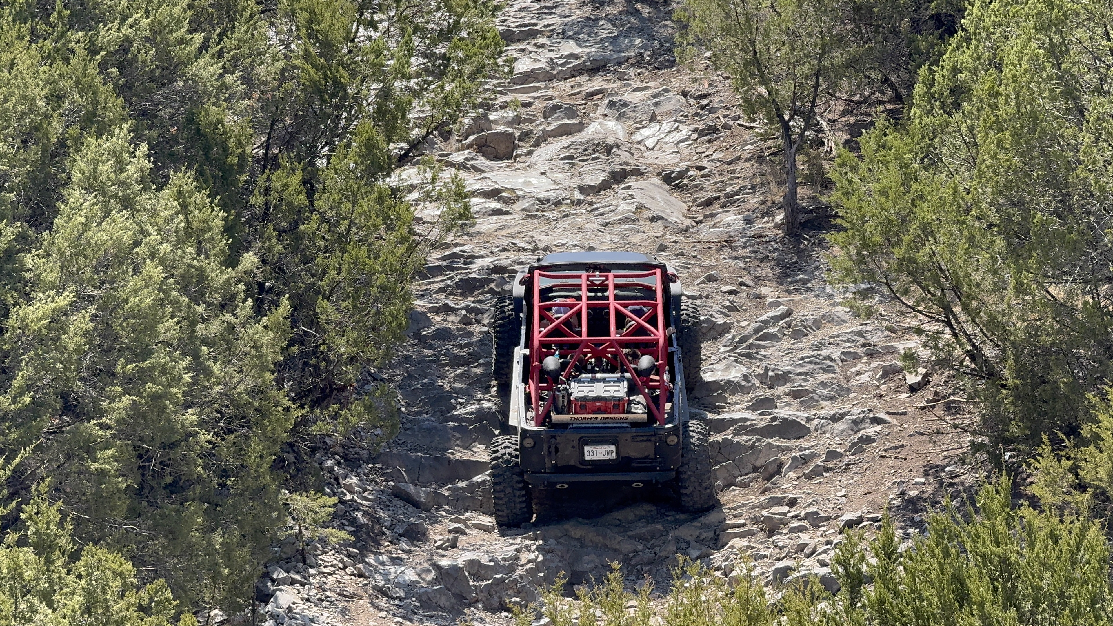 Rear view of a custom Jeep with a red tube cage climbing a rocky trail
